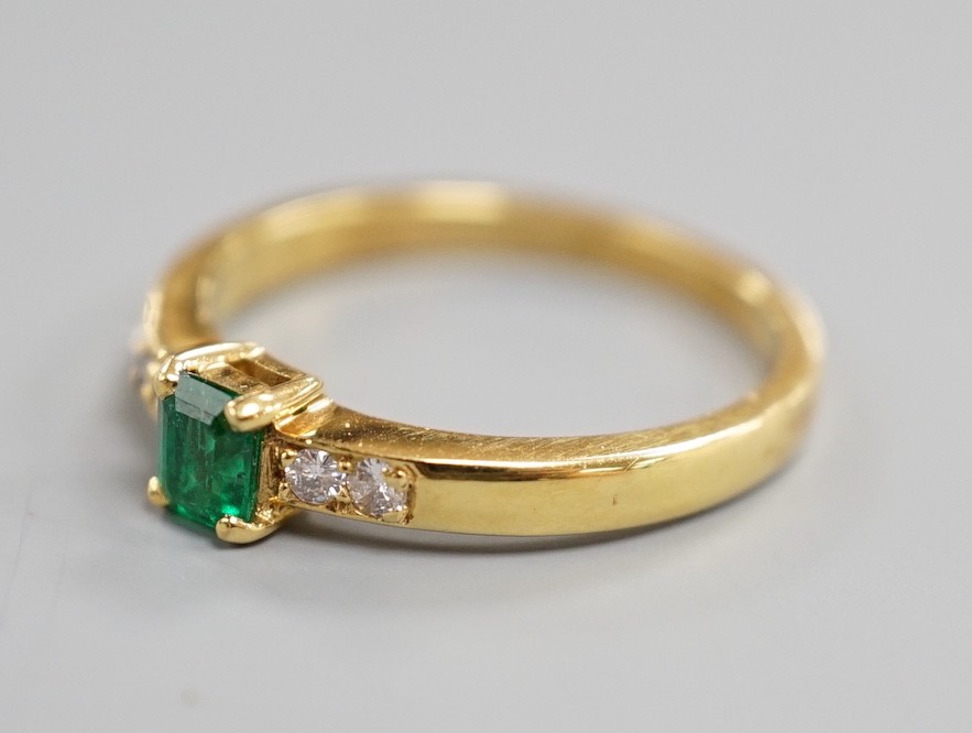 A modern 18ct gold and single stone emerald set ring, with four stone diamond set shoulders, size O, gross weight 3.4 grams